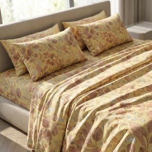 Puede incluir: Una cama está hecha con un juego de sábanas amarillas con estampado floral. El juego incluye una sábana bajera, una sábana encimera y varias fundas de almohada. El estampado floral presenta hojas y tallos marrones y plateados.