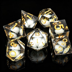 Peut inclure: Ensemble de sept dés polyédriques en résine transparente avec des chiffres dorés et des paillettes blanches internes. Les dés sont conçus pour les jeux de rôle sur table. Chaque dé a une forme géométrique différente.