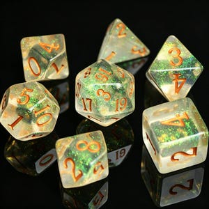 May include: A collection of seven clear, glitter-filled polyhedral dice with orange numbering. The dice are in various shapes, including a d4, d6, d8, d10, d12, and d20. The dice are presented on a reflective black surface.