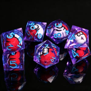 Può includere: Un set di dadi poliedrici realizzati in resina viola traslucida, ognuno contenente un oggetto sferico in miniatura rosso e bianco con una fascia nera. I numeri sui dadi sono incisi in un blu ciano brillante, offrendo un netto contrasto con il viola e i disegni sferici interni.