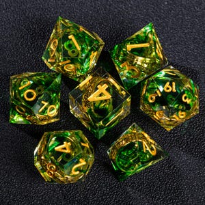 May include: Set of seven polyhedral dice with a green and gold color scheme. The dice are transparent with gold-colored numbers. The dice are designed for role-playing games and are arranged on a dark surface.
