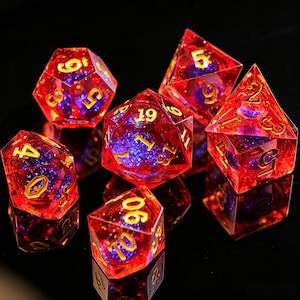 Op de afbeelding: Set van zeven polyhedrale dobbelstenen voor rollenspellen. De dobbelstenen zijn transparant rood met gouden cijfers en een paarse en blauwe glitter binnenkant. Ze liggen op een reflecterend zwart oppervlak.