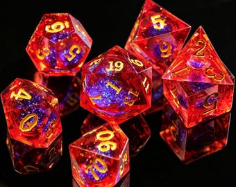 May include: A set of seven polyhedral dice for role-playing games. The dice are transparent red with gold numerals and a purple and blue glitter core. They are displayed on a reflective black surface.