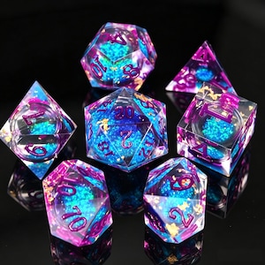 Puede incluir: Juego de siete dados poliédricos con un diseño de galaxia. Los dados son transparentes con detalles en azul, morado y dorado. Cada dado tiene una forma geométrica diferente y numeración morada.