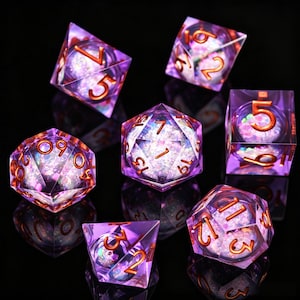 Può includere: Un set di sette dadi poliedrici di varie forme, ciascuno con un esterno viola trasparente e un interno scintillante. I numeri sono color rame. I dadi sono disposti su una superficie nera, riflettendo le loro forme.