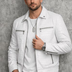 Puede incluir: Chaqueta de cuero blanca con estampado de cocodrilo, cierre de cremallera y bolsillos. Se combina con una camiseta y pantalones blancos. Un reloj y collar plateados completan el look. Elegante prenda de abrigo.