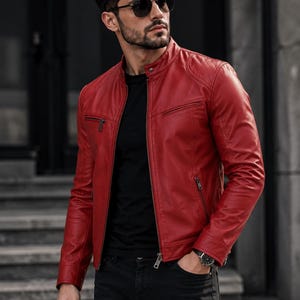 May include: A vibrant red leather jacket featuring a mandarin collar, a full-length front zip, and two zipped chest pockets. The jacket includes quilted shoulder detailing, long sleeves with zipped cuffs, and a smooth, fitted silhouette.