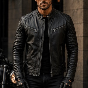May include: A black leather jacket featuring a quilted pattern on the shoulders and sleeves, a stand-up collar with a snap button, two zippered chest pockets, and two lower zippered pockets. The jacket is paired with black leather gloves.