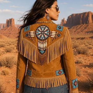 May include: A tan suede jacket featuring long fringe along the back yoke and hem. The back is decorated with a large circular beaded medallion in blue, red, and white, accented by hanging white beads. Similar beaded geometric patches adorn the sleeves.