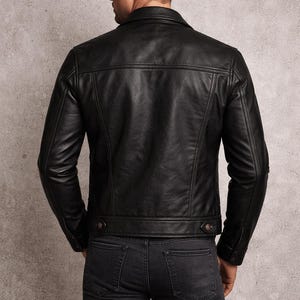 May include: A black leather jacket with a classic design, featuring a collared neckline, buttoned cuffs, and a tailored fit. The jacket is paired with dark gray denim jeans. The model is viewed from the back, showcasing the jacket's details.