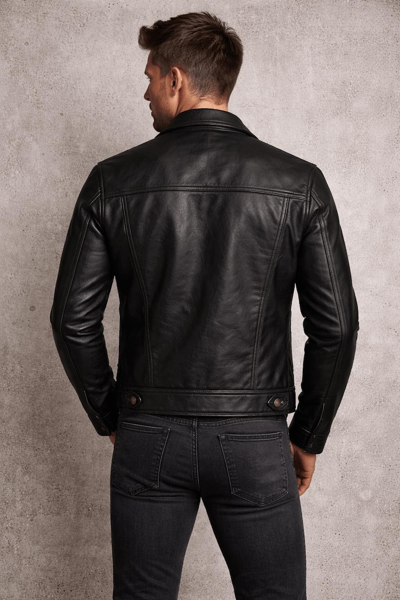 May include: A black leather jacket with a classic design, featuring a collared neckline, buttoned cuffs, and a tailored fit. The jacket is paired with dark gray denim jeans. The model is viewed from the back, showcasing the jacket's details.