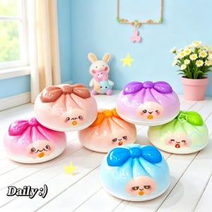 Puede incluir: Una colección de coloridos bollos bao de estilo caricatura con lazos en la parte superior y caras bonitas. Los bollos son en tonos rosa, naranja, morado, verde y azul. La palabra "Daily:)" está en la esquina inferior izquierda.