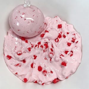 Può includere: Primo piano di slime rosa con granelli rossi a forma di cubo. Una grande palla rotonda dello stesso slime rosa è sopra. Lo slime è in una ciotola bianca.