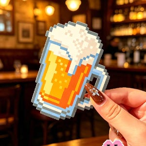 Może przedstawiać: Naklejka w stylu pixel art przedstawiająca kufel piwa wypełniony złotym płynem z białą pianą na wierzchu. Naklejka ma niebieski kontur i jest opatrzona napisem A pitcher of beer u góry oraz Puff Bead Patterns u dołu.