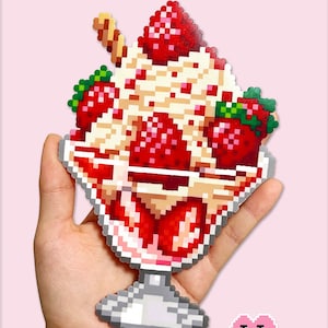 Puede incluir: Un parfait de fresa pixelado, sostenido en una mano, con capas de crema, fresas y una barquilla. El texto "Large Strawberry Parfait" está en la parte superior. La esquina inferior derecha tiene el texto "Puff Bead + Patterns".