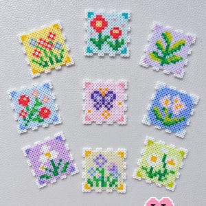 Op de afbeelding: Een verzameling kleurrijke, vierkante mini-spiegels met bloemmotieven. Elke spiegel heeft een uniek ontwerp van bloemen, bladeren of een vlinder, gemaakt met kleine, kleurrijke kralen. De tekst "Mini Floral Mirror - Spring" staat bovenaan.