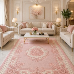 May include: A luxurious living room featuring a large pink floral patterned rug. The room includes cream-colored sofas, a marble coffee table, and a crystal chandelier. The walls are painted in a soft cream color, creating an elegant atmosphere.