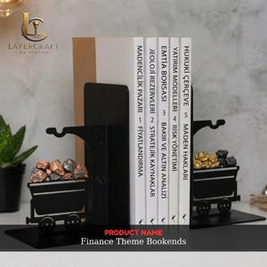 Pode incluir: Um par de suportes para livros em metal preto com um design de vagoneta de mina cheia de pedras em tons metálicos. Os suportes sustentam cinco livros brancos com texto preto nas lombadas, incluindo títulos como Madencilik Pazari e Hukuki Çerçeve.