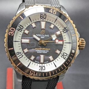 Op de afbeelding: Breitling Superocean Chronometer polshorloge met zwarte wijzerplaat, gouden accenten en een zwarte rubberen band. Het horloge heeft een draaibare bezel met witte cijfers. Waterdicht tot 300m. De wijzerplaat toont het Breitling-logo.