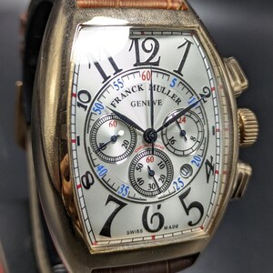 May include: A Franck Muller Geneve chronograph watch with a tonneau-shaped gold case, a white guilloch&eacute; dial featuring black Arabic numerals, three sub-dials, and a brown leather strap with a textured crocodile pattern and a gold-tone buckle.