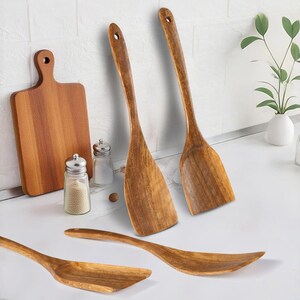 May include: A collection of wooden kitchen utensils, featuring spatulas, a chopping board, and serving spoons. The light brown wooden items are displayed on a white surface. Salt and pepper shakers are also present.