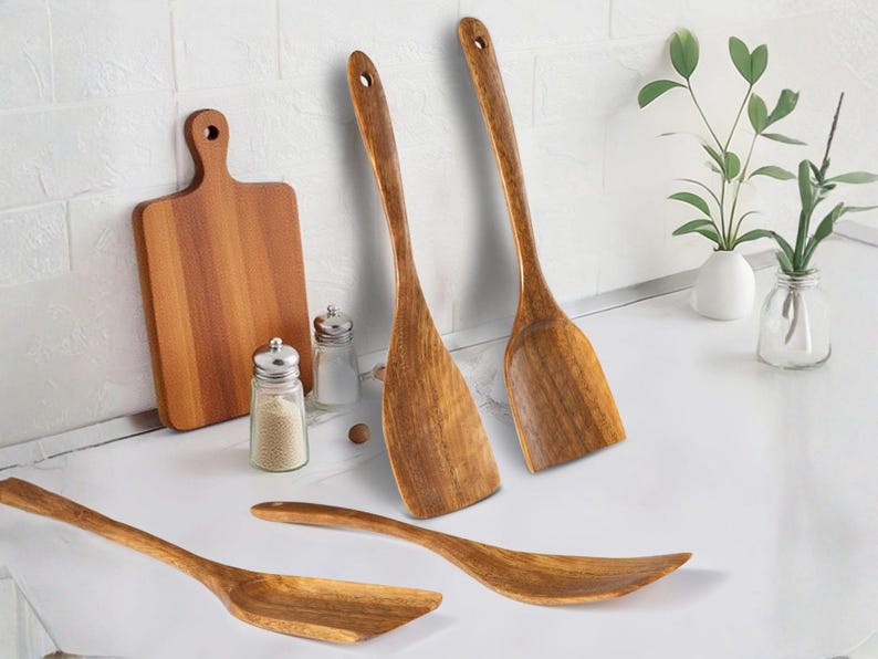 May include: A collection of wooden kitchen utensils, featuring spatulas, a chopping board, and serving spoons. The light brown wooden items are displayed on a white surface. Salt and pepper shakers are also present.