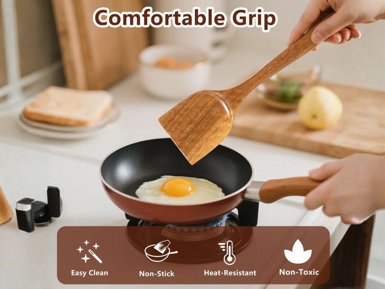 May include: A wooden spatula with a rectangular head is held over a small red and black frying pan with a fried egg. The image includes the text "Comfortable Grip", "Easy Clean", "Non-Stick", "Heat-Resistant", and "Non-Toxic".
