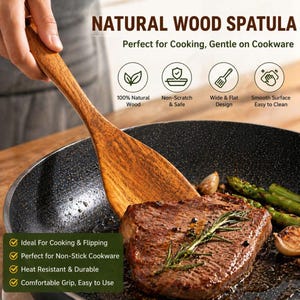 May include: A wooden spatula is shown in use, flipping a steak in a non-stick pan. The spatula is made of light brown wood and has a wide, flat design. The pan contains cooked steak, asparagus, and lemon slices.