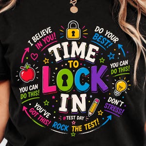May include: Black t-shirt with a colorful graphic design. The design includes the words "TIME TO LOCK IN" with supporting phrases like "I believe in you!" and "Rock the test!" along with a pencil, apple, and lightbulb.