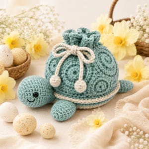Puede incluir: Una bolsa de ganchillo en forma de tortuga de color verde azulado con un caparazón texturizado de patrones en espiral, un cordón color crema con dos extremos esféricos pequeños y una cabeza redondeada con ojos de cuentas negras.
