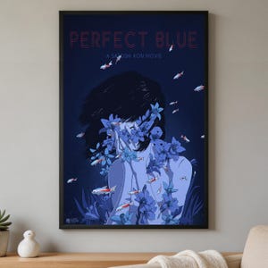 K&ouml;nnte beinhalten: Ein gerahmtes Filmplakat f&uuml;r Perfect Blue von Satoshi Kon mit dunkelblauem Hintergrund, einer zentralen Figur, die von blauen Blumen verdeckt wird, und kleinen schwimmenden Fischen. Der Text Perfect Blue und A Satoshi Kon Movie steht oben in Rot.