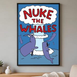 May include: A framed wall art print featuring a blue background with a central white mushroom cloud. The red text reads NUKE THE WHALES. Several purple whales are depicted swimming in the water below the cloud, with smaller whales in the distance.