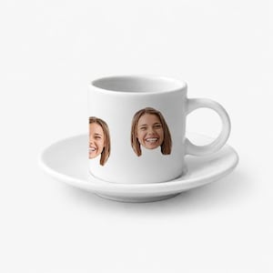 Puede incluir: Una taza de espresso de cerámica blanca con su plato a juego. La taza presenta un estampado gráfico repetido del rostro de una persona sonriente con cabello castaño claro, situado alrededor de la superficie exterior del recipiente blanco.