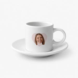 Może przedstawiać: Biała ceramiczna filiżanka do espresso z pasującym spodkiem. Na przedniej części filiżanki znajduje się wyśrodkowana grafika w kształcie jasnoróżowego serca, zawierająca fotograficzny portret uśmiechniętej osoby z brązowymi włosami do ramion.