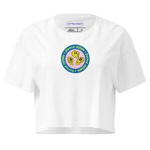 Puede incluir: Top corto blanco con un gráfico circular que presenta tres emoticonos amarillos derritiéndose dentro de un anillo azul con el texto "Dying Inside". La camiseta tiene una pequeña etiqueta que dice "Dimensia".