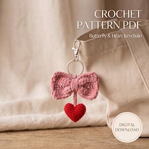 Peut inclure: Un modèle de crochet PDF pour un porte-clés papillon et cœur. Le porte-clés présente un nœud crocheté rose poudré attaché à un anneau en métal argenté et un petit cœur crocheté rouge vif suspendu en dessous. Le texte indique CROCHET PATTERN PDF.