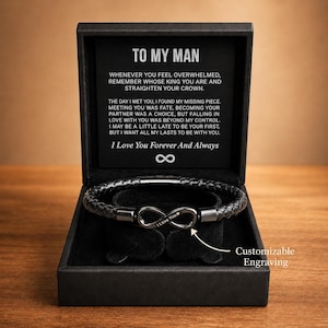 Op de afbeelding: Een zwarte geschenkdoos met een gevlochten leren armband met een oneindigheidssymbool. De doos bevat de tekst "TO MY MAN" en een liefdevolle boodschap. De armband is graveerbaar.
