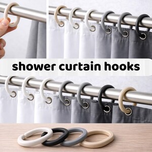 Op de afbeelding: Douchegordijn haken in verschillende kleuren, waaronder wit, grijs, zwart en beige. De haken worden getoond op een metalen stang met witte, grijze en zwarte douchegordijnen. De tekst "shower curtain hooks" is afgebeeld.