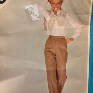 Może przedstawiać: Wzorzec szycia vintage przedstawiający kobietę w białej koszuli i brązowych spodniach. Wzór jest przeznaczony do spodni i zawiera tekst "Koszula i sweter nie są wliczone w cenę".