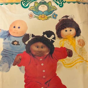 May include: Image of three Cabbage Patch Kids dolls. One doll wears a red onesie, another a blue outfit, and the third a yellow dress. The Cabbage Patch Kids logo is at the top, with the number 6507.