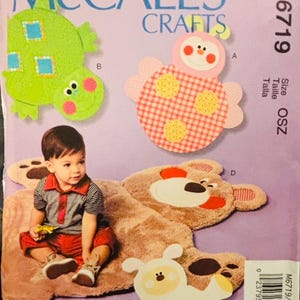 May include: A McCall's Crafts sewing pattern, M6719, featuring plush animal designs. The pattern includes a green dinosaur, a pink and red ladybug, a white sheep, and a large brown bear. A child is sitting on the bear. The pattern is size OSZ.