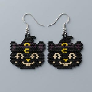 May include: A pair of beaded earrings shaped like black cat heads wearing purple witch hats. The cats feature yellow crescent moon symbols on their foreheads, cream-colored eyes and mouths, and yellow noses. The earrings hang from silver-toned metal hooks.