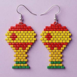 May include: A pair of beaded earrings shaped like a trophy, constructed from small red, yellow, and green cylindrical beads. The design features a red top section, a yellow middle, and a green base, suspended from silver-toned metal earring hooks.
