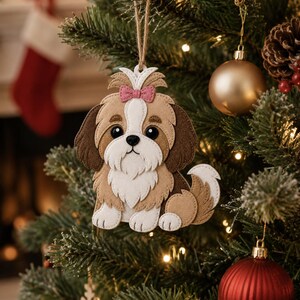 May include: A felt Shih Tzu dog Christmas ornament with a pink bow, hanging on a decorated Christmas tree. The ornament is brown, white, and tan, with black eyes and a fluffy tail. The background includes a fireplace and other ornaments.