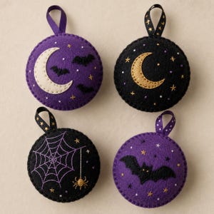 May include: Four round felt ornaments featuring embroidered designs. One purple with a cream moon and bats, one black with a gold moon and stars, one black with a purple spiderweb and spider, and one purple with a black bat and gold stars.