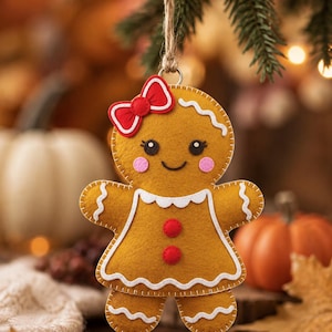 May include: A felt gingerbread person ornament featuring a brown body, a red bow on its head, pink cheeks, and a white scalloped collar and trim. The figure has two red circular buttons on its torso and is suspended by a brown twine loop.