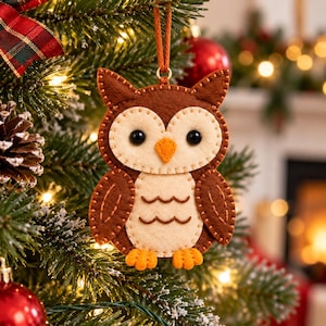 May include: A felt owl ornament featuring dark brown wings and head, a cream-colored face and belly, black bead eyes, an orange triangular beak, and orange feet. The owl is constructed with visible brown stitching and hangs from a brown cord.