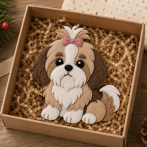 May include: A felt Shih Tzu dog ornament with brown, white, and tan colors, a pink bow, and large black eyes. The dog is inside a brown cardboard box filled with shredded paper. A festive holiday theme.