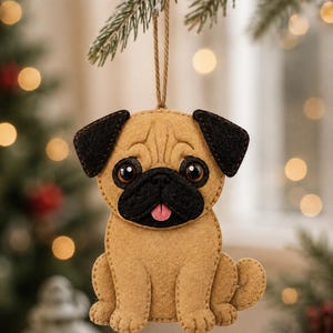 May include: A tan and black felt pug ornament featuring a sitting dog with large dark eyes, a black muzzle, and a small pink tongue. The ornament is constructed from layered felt pieces with visible stitching and hangs from a thin brown twine loop.