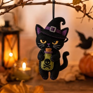 May include: A black felt cat ornament wearing a purple-banded witch hat and holding a light green potion bottle with a cork stopper. The bottle features a black skull and crossbones graphic. The cat has yellow eyes, a purple nose, and white whiskers.
